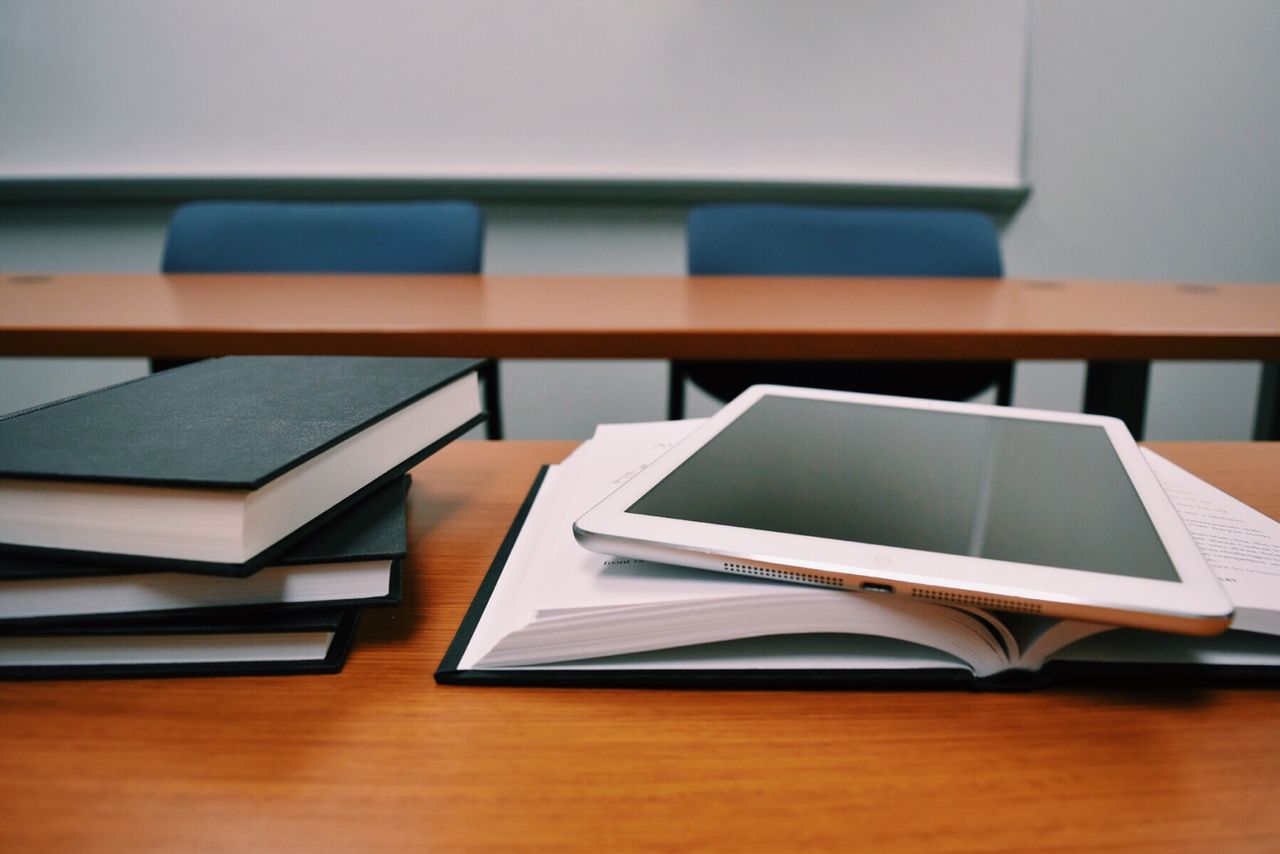 Services Books and a tablet on a desk in a classroom, depicting modern education.