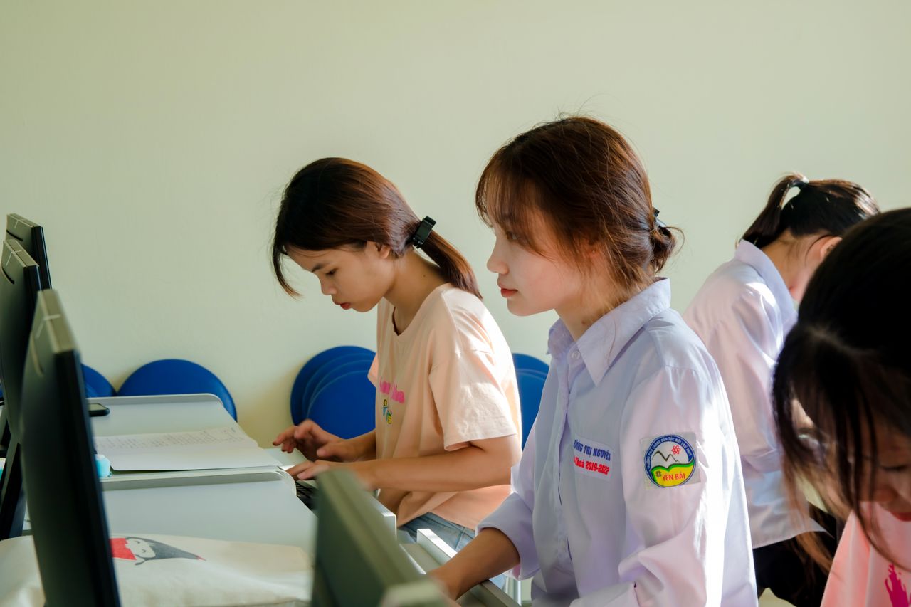 Services Three young women concentrating on a computer task in a classroom setting.