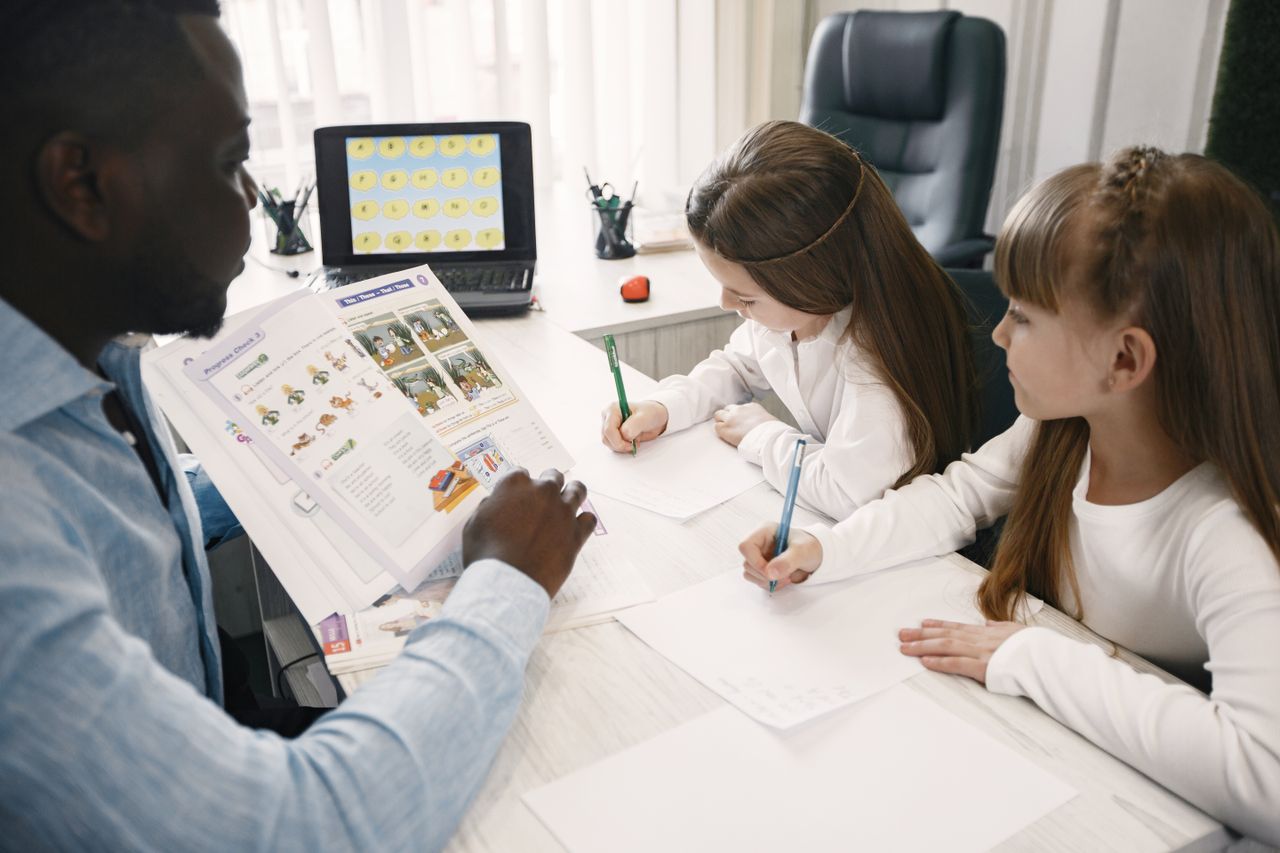 Home A teacher instructing two young students in a classroom environment.