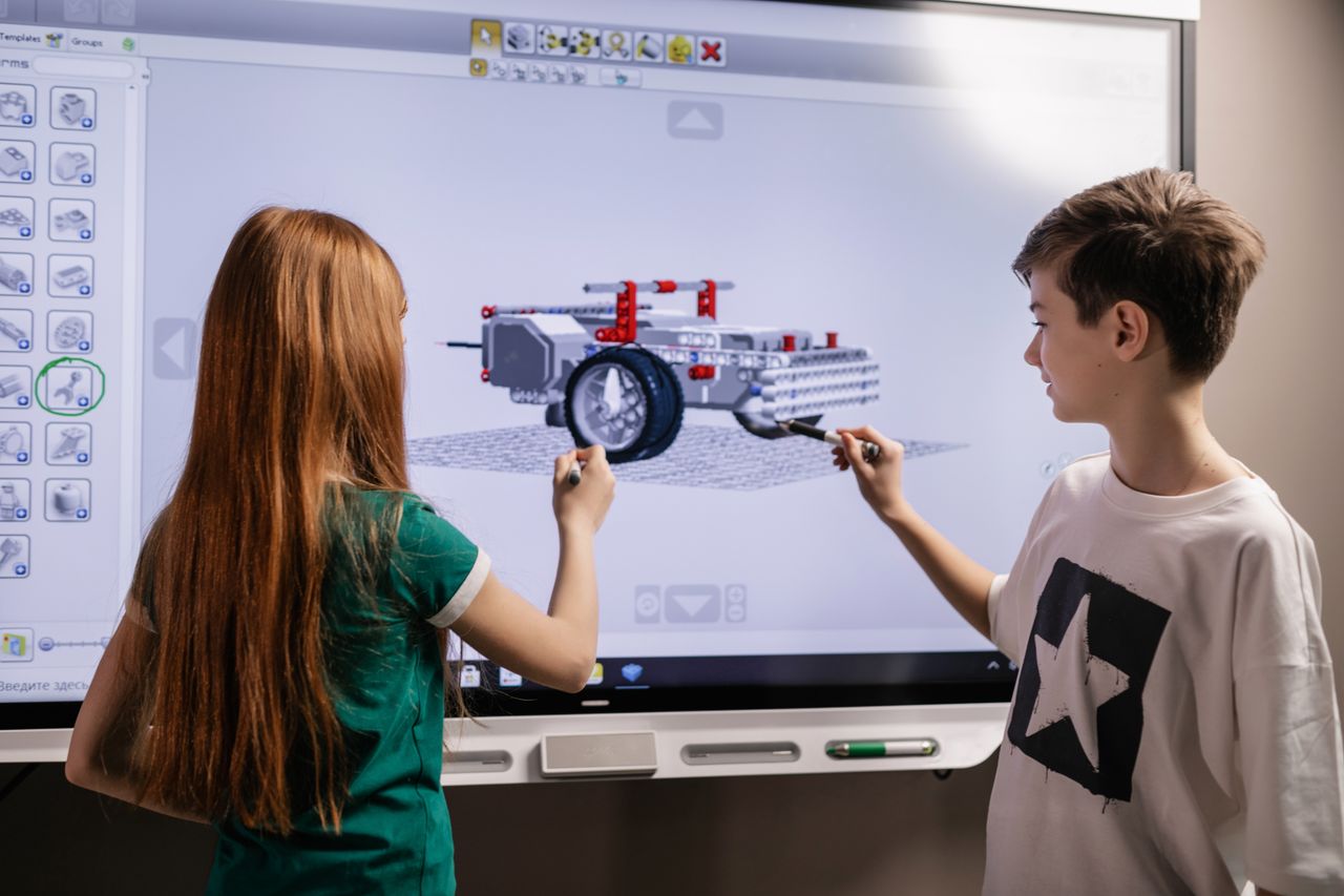 Home A boy and girl collaborate on a robotics project using a digital screen in a classroom setting.