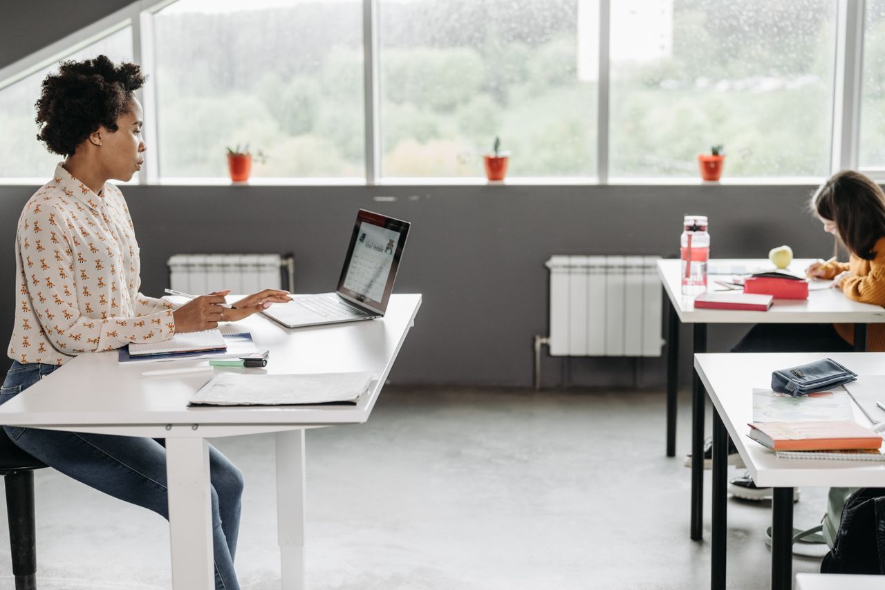 Home A teacher focused on her laptop in a bright, modern classroom setting.